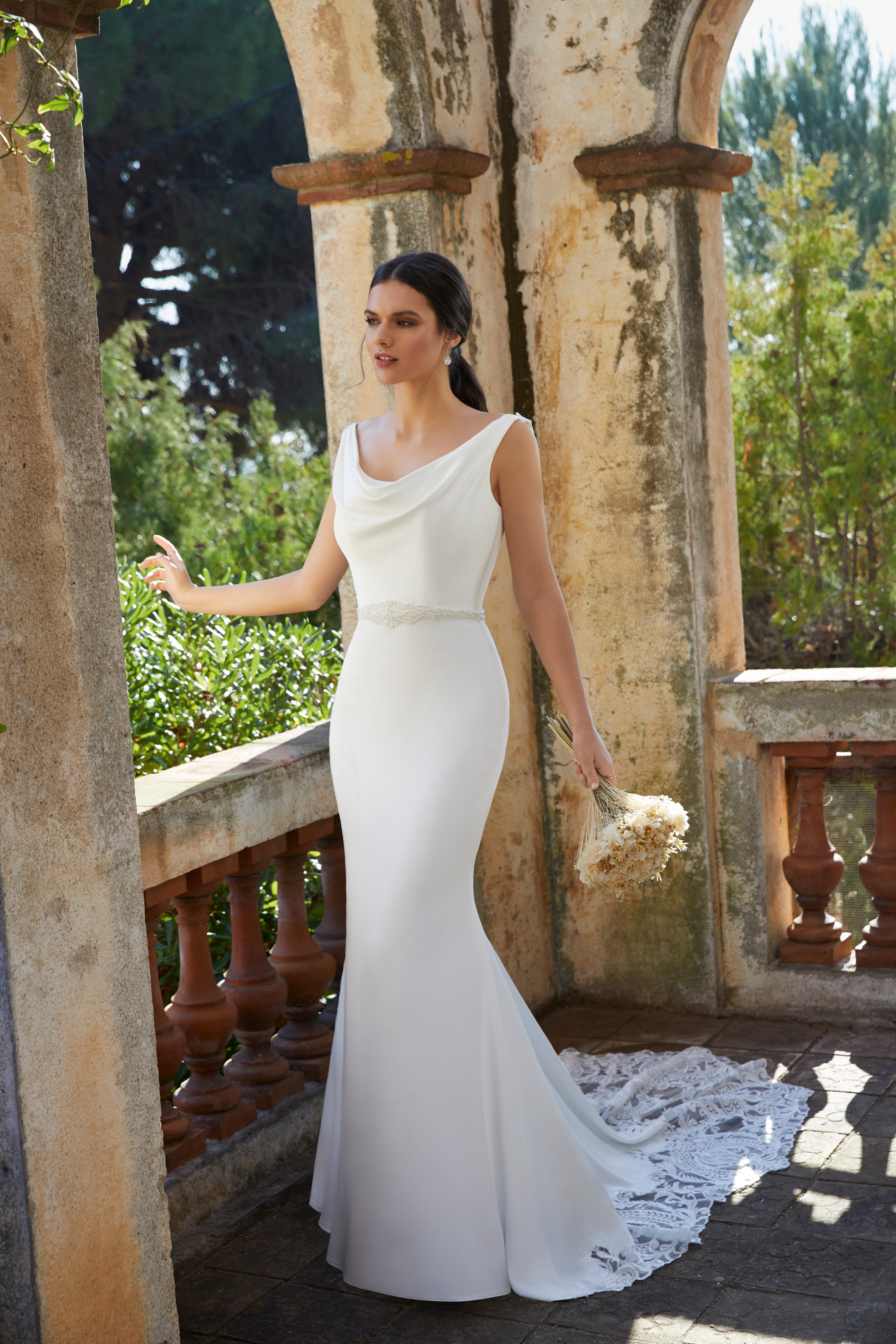 Model stood outside wearing Ronald Joyce Victoria Jane style 18466, an elegant crepe wedding gown with a cowl neck that’s perfect for small weddings 