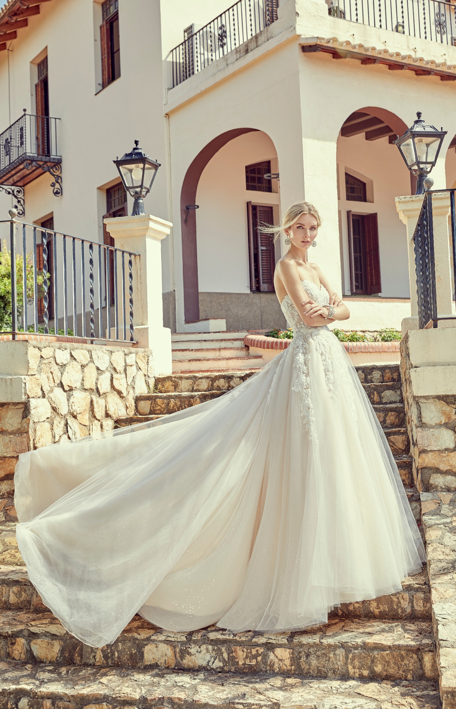 Model stood outside a block of white villas wearing Ronald Joyce wedding dress style 69407, an ivory strapless A-line dress with a sparkle tulle skirt
