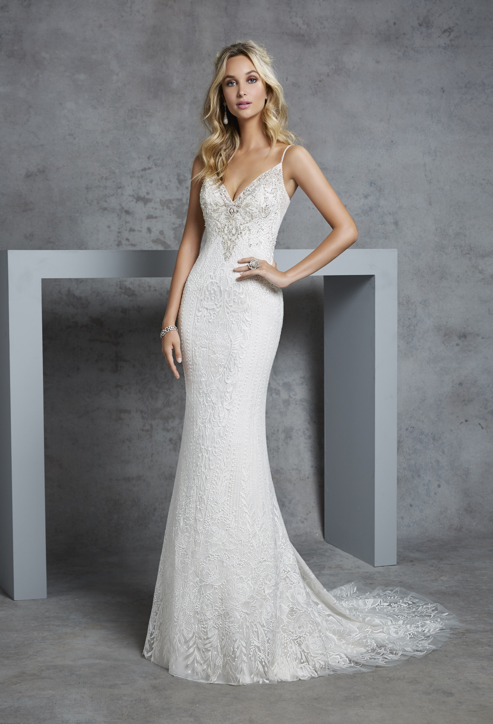 Model in Ronald Joyce 69409, a lace sheath wedding dress silhouette with delicate beaded straps, a silver beaded bust, modern v-neckline and lace puddle train