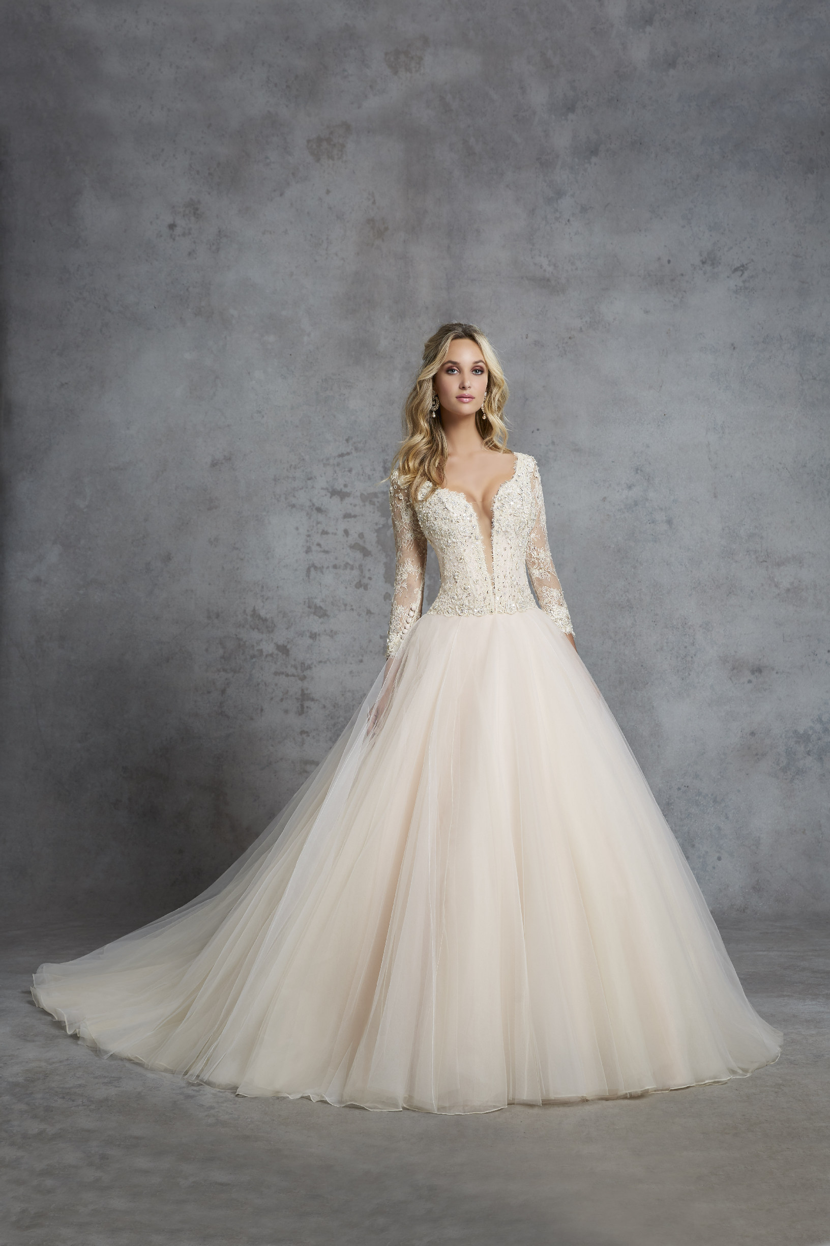 Model in Ronald Joyce 69424, a pale gold ballgown wedding dress silhouette with a sequin lace body, plunging v-neckline, long lace sleeves and a plain tulle skirt
