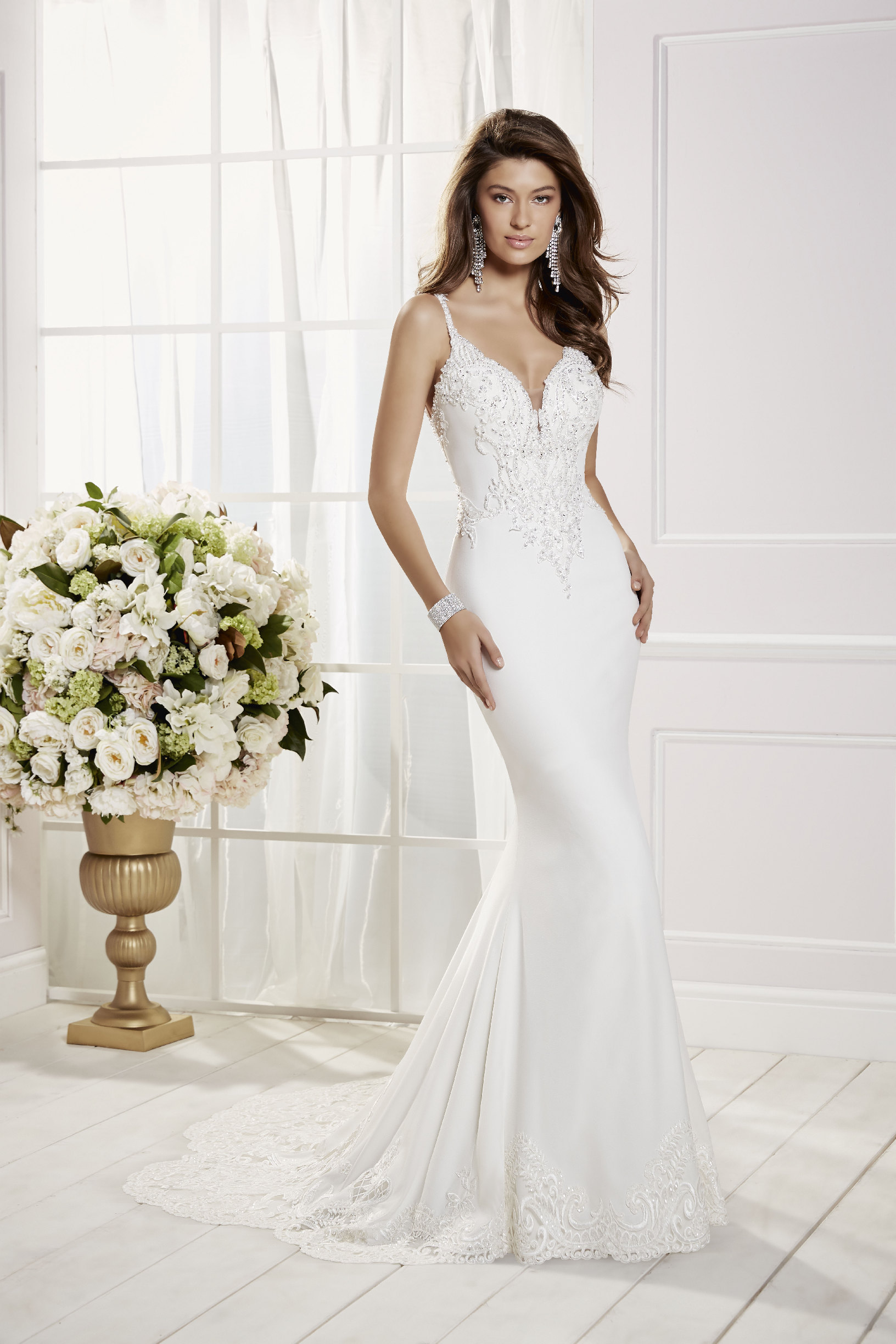 Model stood in a white room near cream flowers in Ronald Joyce 69458, a fishtail wedding dress with a beaded sweetheart neckline, delicate straps, a plain skirt and lace hem