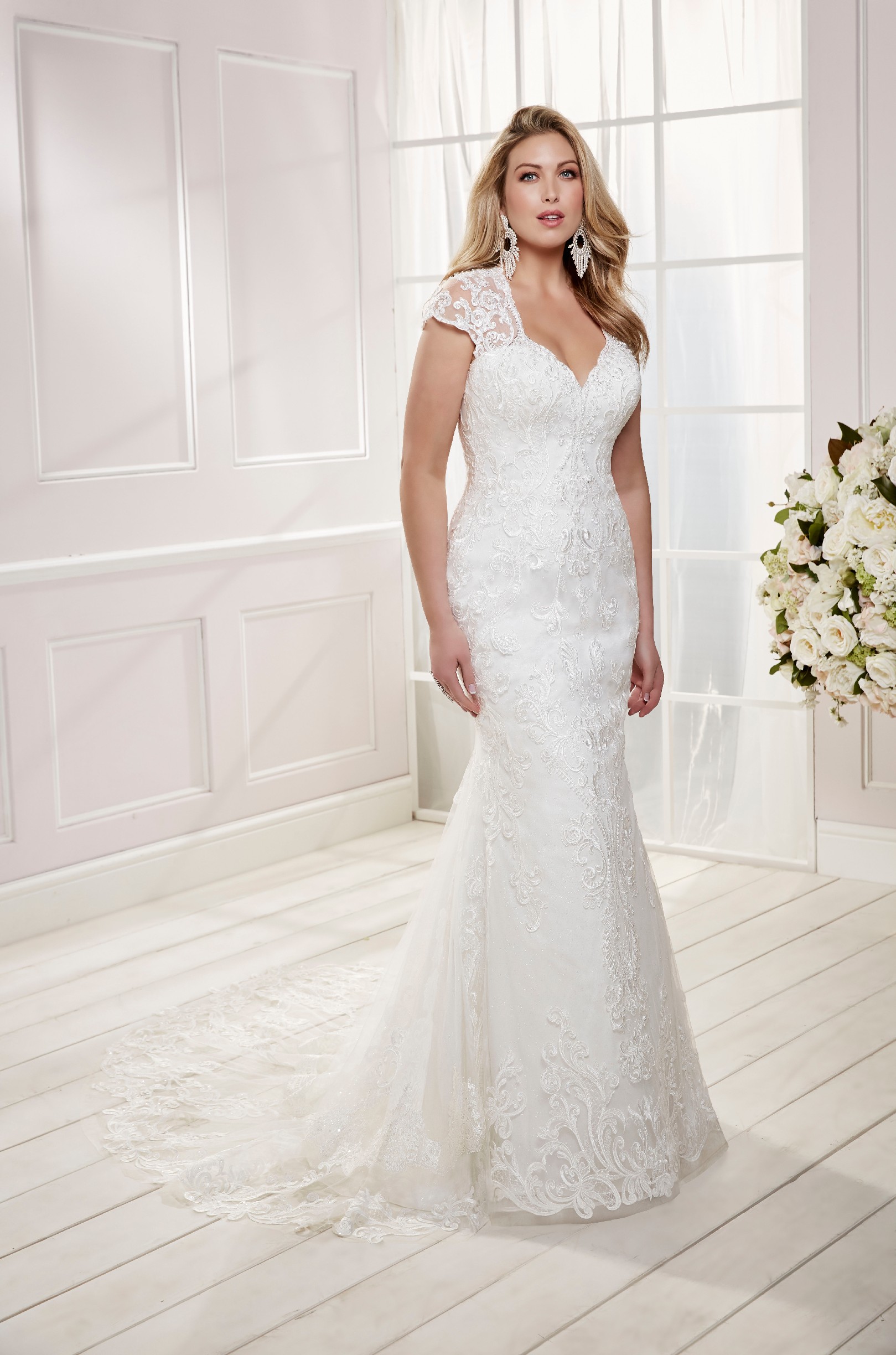 Curvy model in Ronald Joyce plus size wedding dress style 69473, an ivory fit and flare dress with capped sleeves and lace appliques 