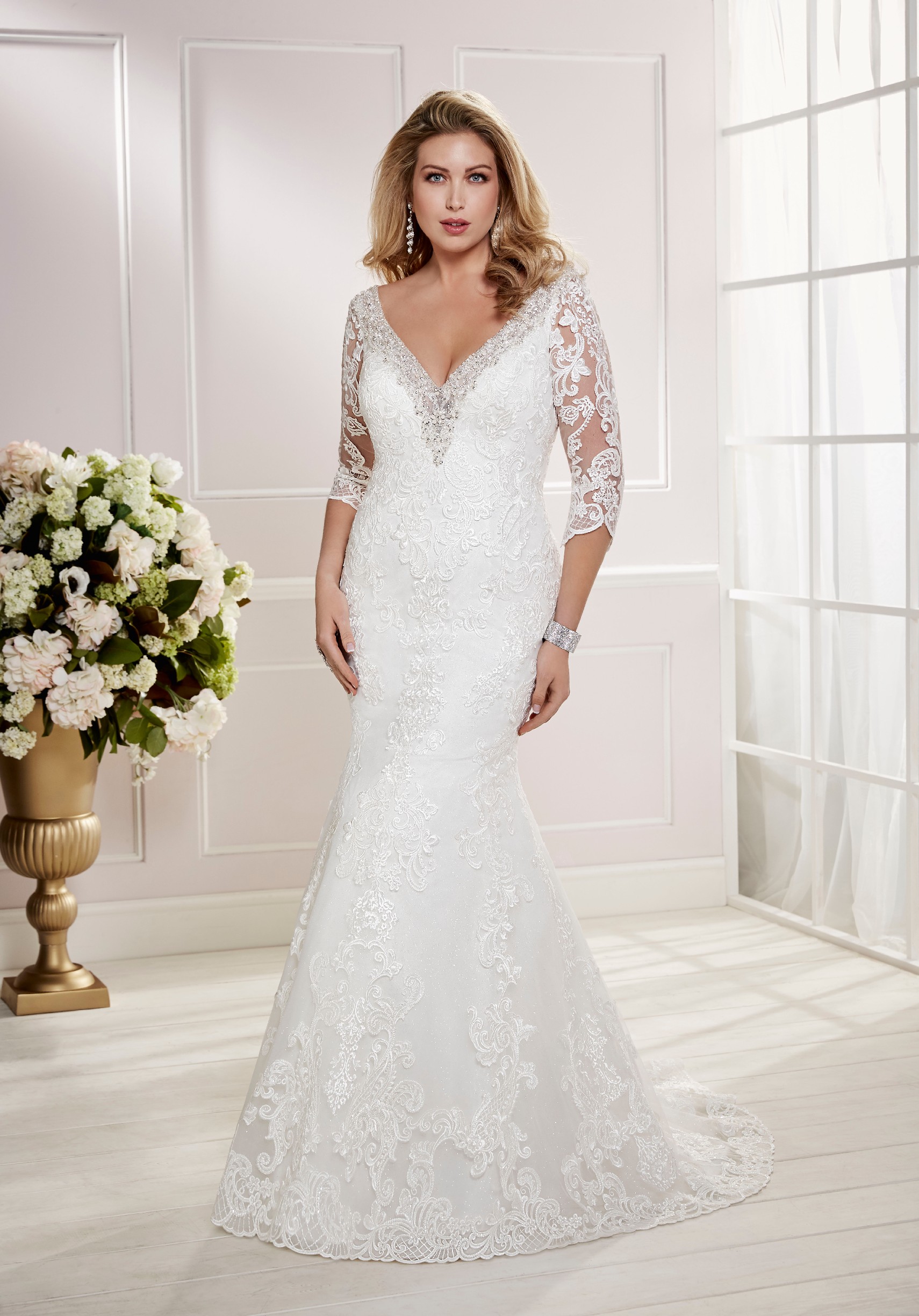 Curvy model in Ronald Joyce plus size wedding dress style 69474, an ivory fit and flare dress with lace illusion 3/4 sleeves and a plunging neckline edged with beading 