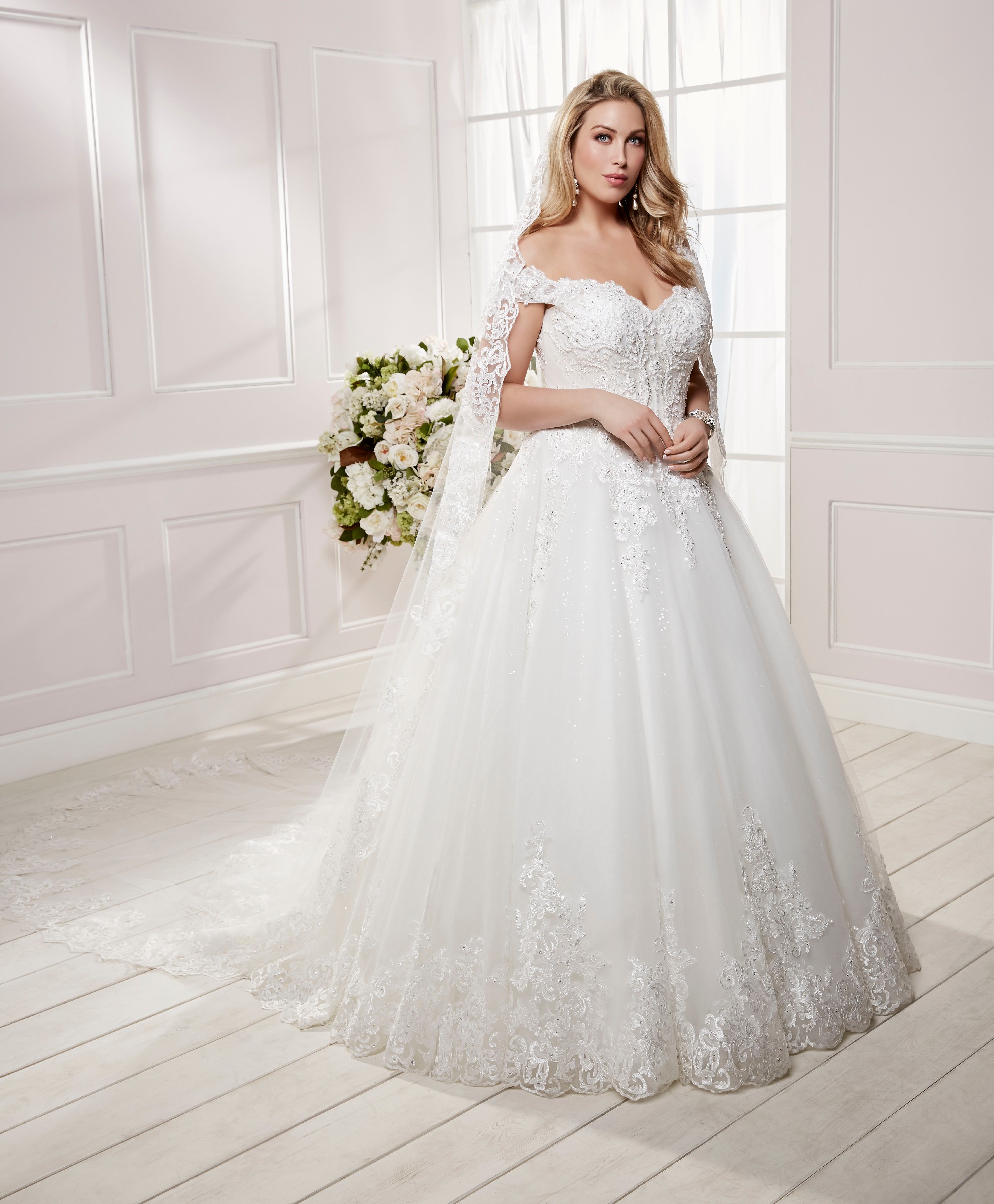 Curvy model in Ronald Joyce plus size wedding dress style 69479, an ivory tulle ballgown dress with detachable off-the-shoulder cap sleeves and lace appliques  