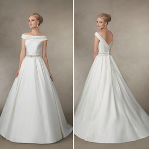 Blonde model stood against a grey backdrop in Ronald Joyce 18013, a plain off the shoulder Mikado wedding dress fit for a princess. Dress has a sparkle belt and open back.